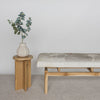 front view of a gray and caramel hide on a cowhide bench seat secured to a teak wood base by Corcovado Designs  together with a small wooden side table and eucalyptus leaves