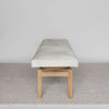 end view of a Corcovado large creamy white cowhide bench seat on a teak wood base.