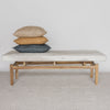 front view of 3 cushions on a large creamy white cowhide bench seat on a teak wood base.