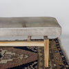 close up of the end of a Corcovado Design creamy white cowhide bench seat with wooden legs on a vintage turkish rug