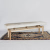 angled view of a Corcovado Design creamy white cowhide bench seat with wooden legs on a vintage turkish rug