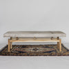 a side view of a Corcovado Design creamy white cowhide bench seat with wooden legs on a vintage turkish rug