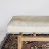 end view of a creamy caramel colored cowhide bench on a teak wood base from Corcovado Designs, placed on a vintage rug