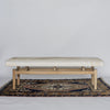 front view of a creamy caramel colored cowhide bench on a teak wood base from Corcovado Designs, placed on a vintage rug