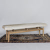 angled view of a creamy caramel colored cowhide bench on a teak wood base from Corcovado Designs, placed on a vintage rug