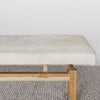 close up end view showing the leather stitching of off-white cowhide bench seat made from a single cowhide and secured to a teak wood base from Corcovado Designs, on a grey large-looped rug