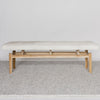 front view of off-white cowhide bench seat made from a single cowhide and secured to a teak wood base from Corcovado Designs, on a grey large-looped rug