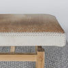 close up view of Corcovado Design's cowhide ottoman bench which featuring caramel and cream shades on top of a looped rug.