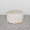 light colored cowhide ottoman coffee table with small teak wood feet and leather stitching detail