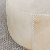 close up of the leather stitching on the light colored cowhide ottoman coffee table with small teak wood feet