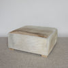 caramel brown and creamy colored square hide ottoman coffee table photographed on an angle