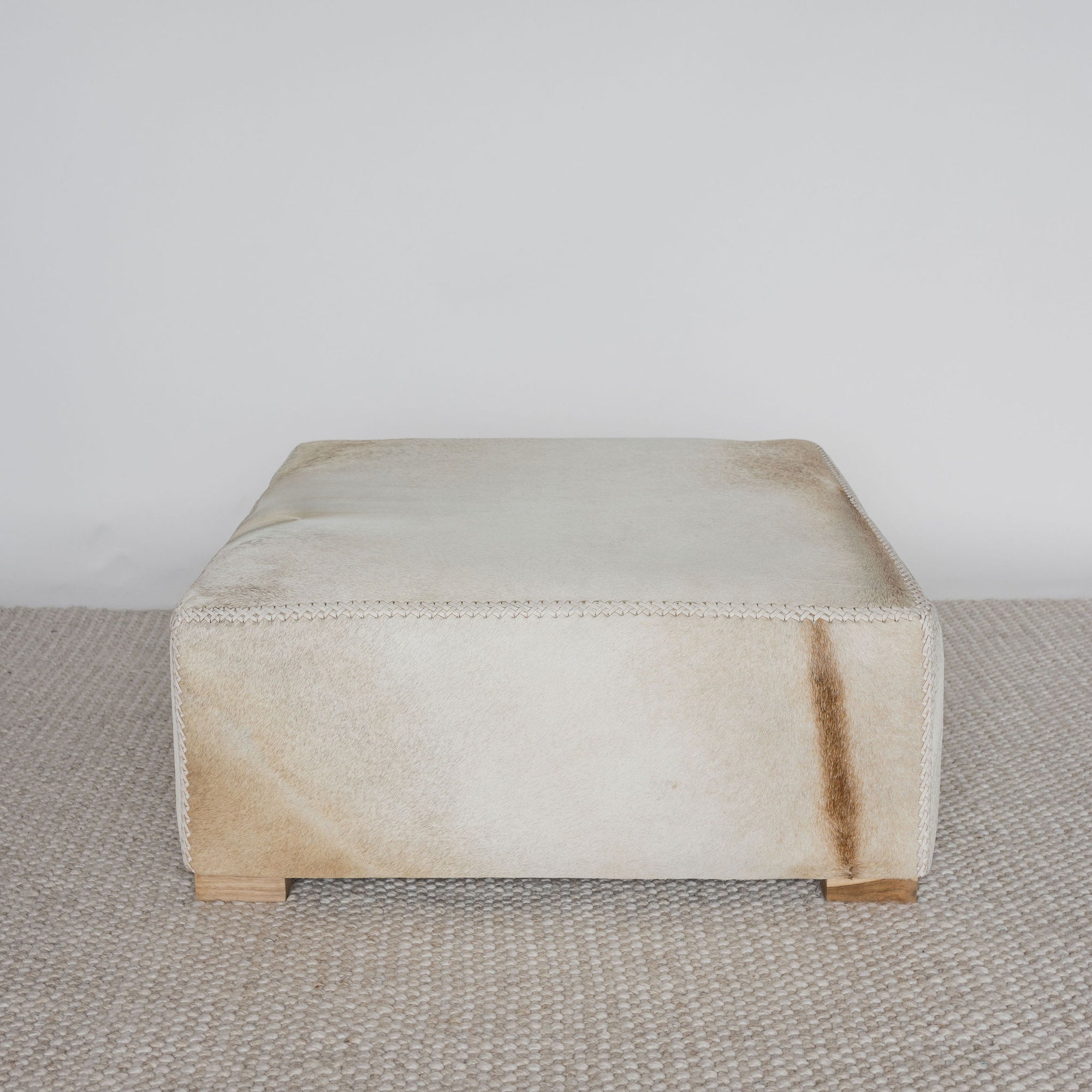 light colored square hair on hide ottoman coffee table with small teak wood feet and distinctive caramel natural marking on one side