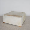 angled view of the light colored square hair on hide ottoman coffee table with small teak wood feet