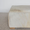 close up view of  the light colored square hair on hide ottoman coffee table with small teak wood feet