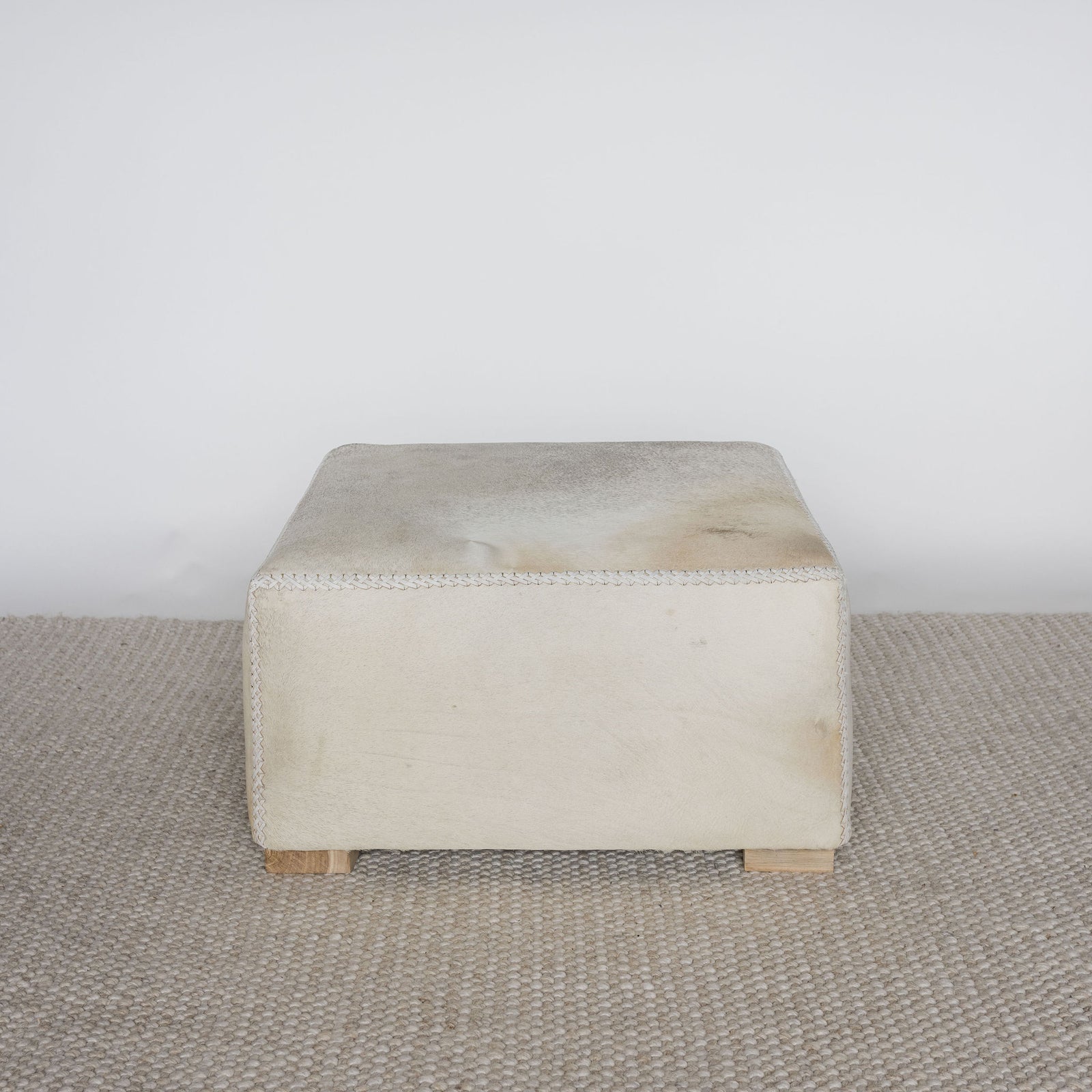square cowhide ottoman coffee table in light tones with small teak wood feet