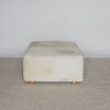 angled view of the square creamy colored cowhide ottoman coffee table