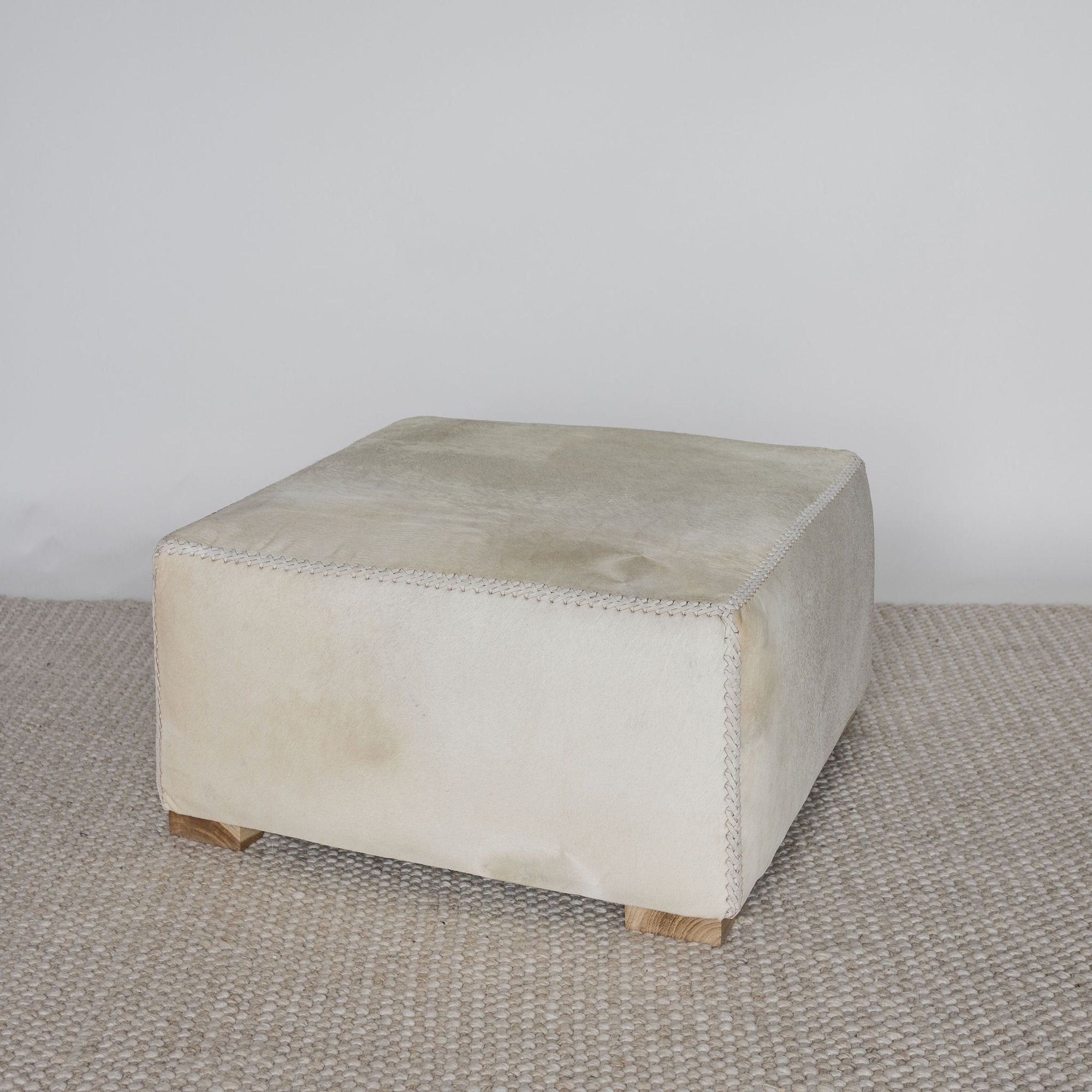 angled view of the square creamy colored cowhide ottoman coffee table 