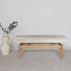 front view of the earthy colored hide on the cowhide bench seat on a teak wood base next to an organic vase