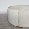 close up view of the leather stitching on the extra large cowhide round ottoman in light colored tones