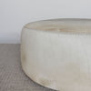 close up of the extra large round hair on hide ottoman coffee table with leather stitching and small teak wood feet on a grey and white rug