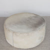 top view of the extra large round hair on hide ottoman coffee table with leather stitching and small teak wood feet on a grey and white rug