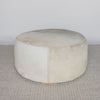 extra large round hair on hide ottoman coffee table with leather stitching and small teak wood feet on a grey and white rug