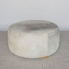 extra large round hair on hide ottoman coffee table with leather stitching and small teak wood feet on a grey and white rug