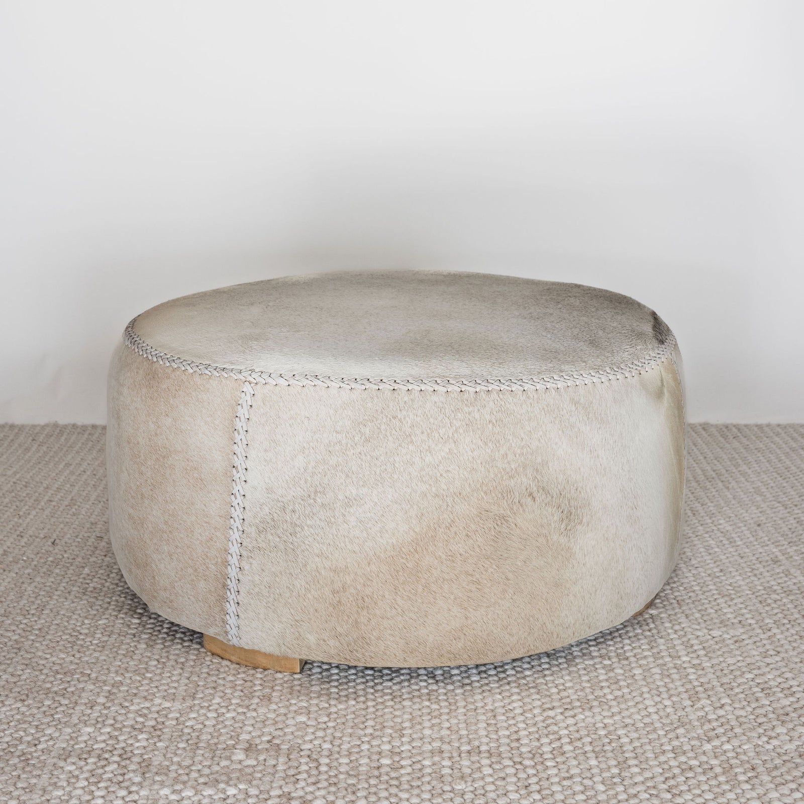 natural toned round hide footstool with leather stitching 