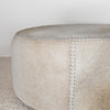 close up photo of the natural toned round hide footstool with leather stitching