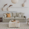 square hair on hide ottoman with a small woven tray on top on a rug and in front of a loose cover sofa