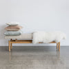 cream boucle upholstered bench seat ottoman for entry or bedroom bench with a pile of cushions and a soft icelandic white sheepskin