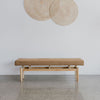 earthy tobacco colored bench seat by corcovado designs beneath rattan art work