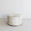 side view of the brown and cream round cowhide ottoman coffee table