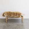 Front view of the brown and cream colored cowhide bench seat with a caramel icelandic sheepskin on top