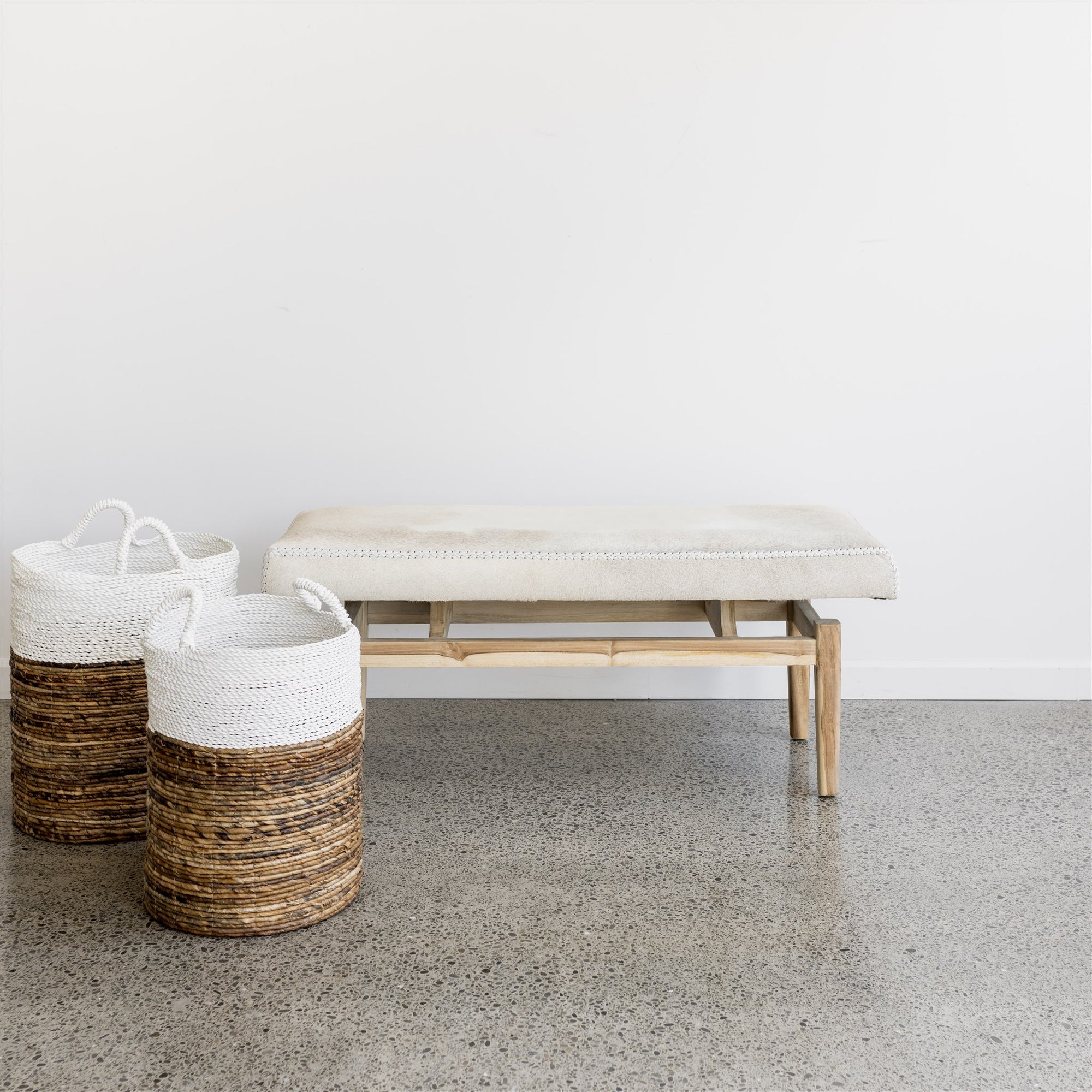 cream colored cowhide bench seat with two woven natural and white baskets beside it