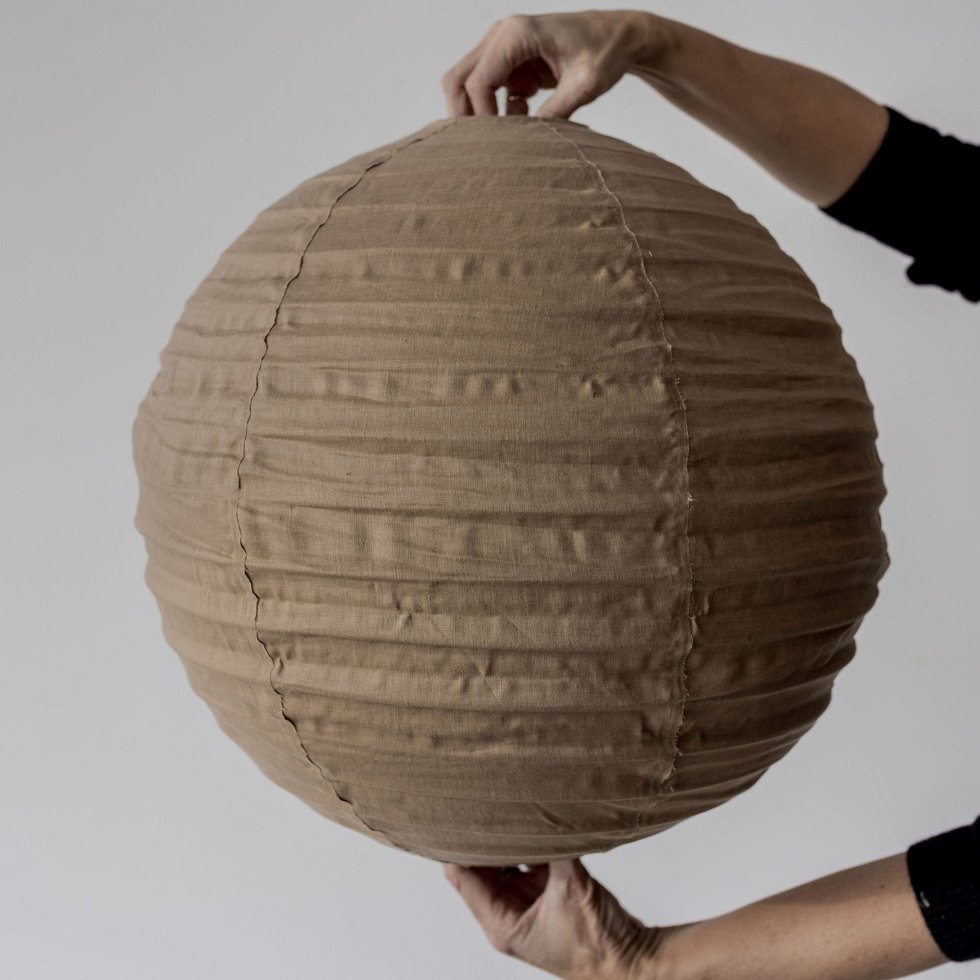 brown round fabric pendant light shade being held by a woman's hands