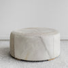 Corcovado Designs round hide ottoman coffee table with a grey stripe and leather stitching placed on a white looped floor rug