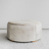 Full side view of Corcovado Designs round hide ottoman coffee table with a grey stripe and leather stitching placed on a white looped floor rug