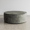 low round green velvet ottoman with piped edges in green velvet on concrete floor