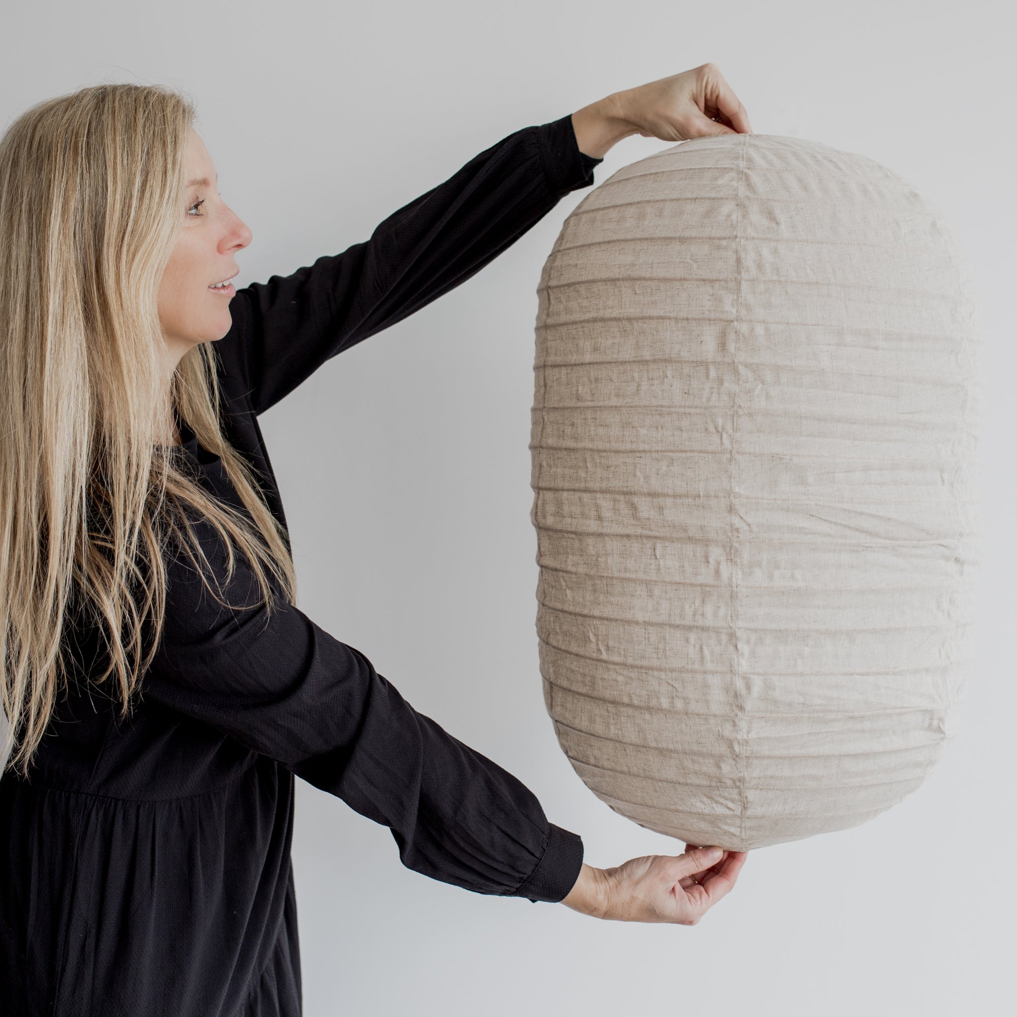 woman holding an oblong shaped linen pendant light shade in natural