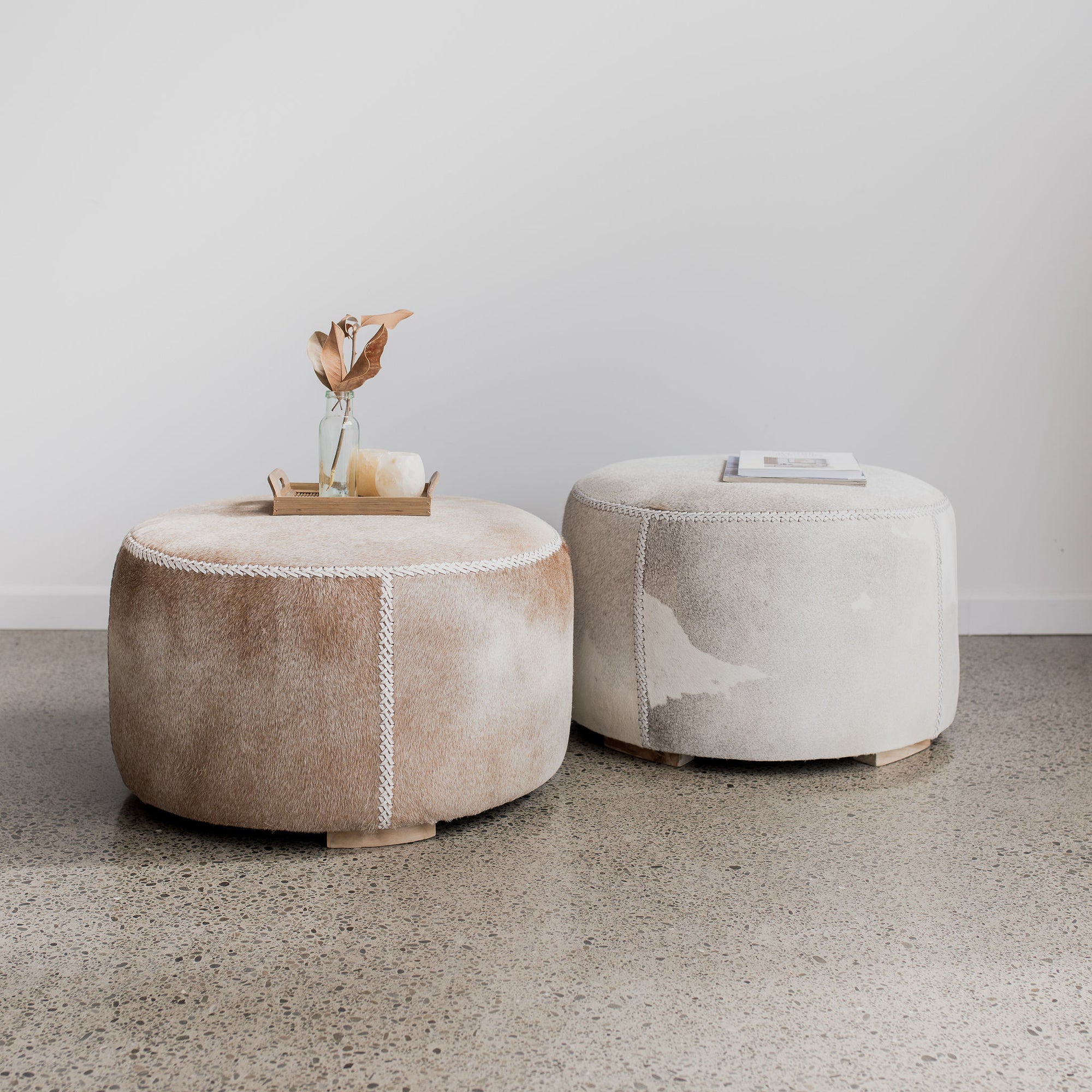 Corcovado caramel colored hide round ottoman next to a gray hide on a round ottoman
